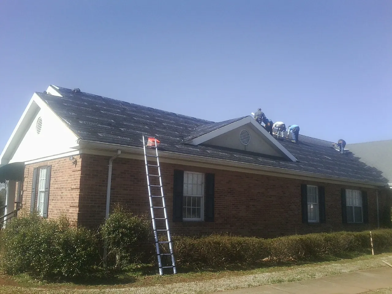 Crew tearing shingles off a brick ranch roof with a ladder set — Metal Roof Repair work by our crew in Pawlet