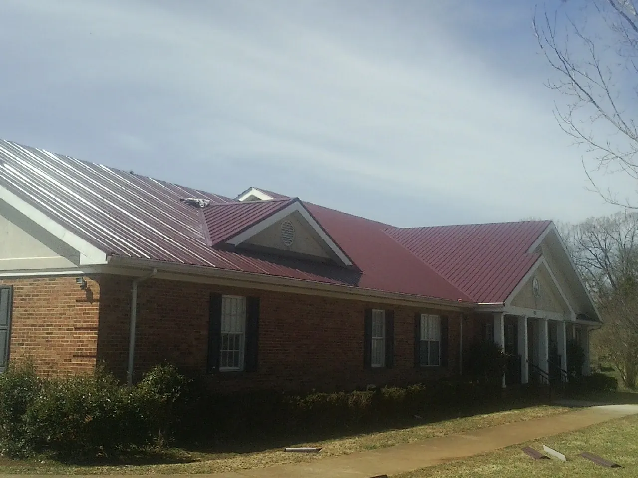 Red metal roof with gabled entries on a long brick building, from a Hail Damage Roof Repair job in Pawlet