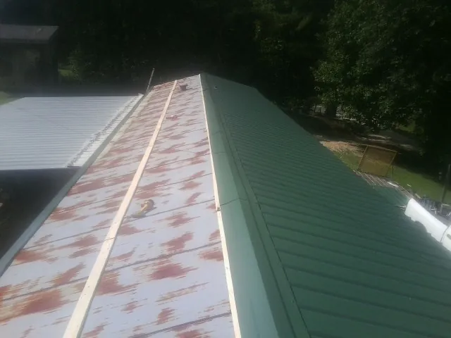 Old rusted panels beside newly installed green metal roofing — Wind Damage Roof Repair by Roofing Brothers in Pawlet