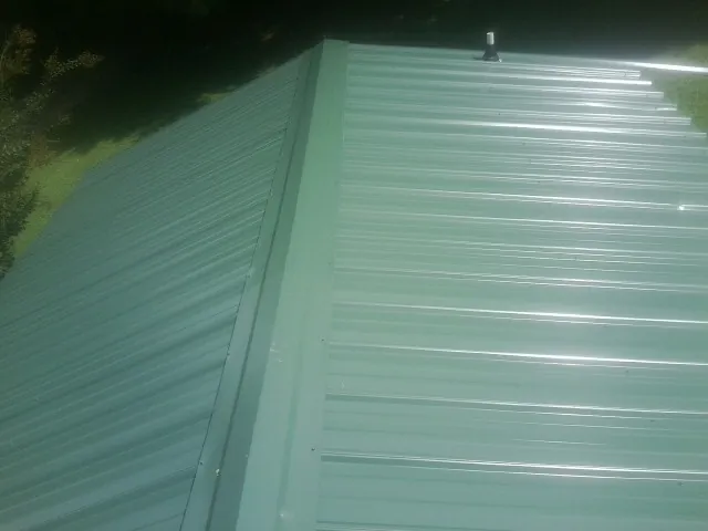 New green metal panels meeting at the ridge of a roof — Flat Roof Repair work by our crew in Pawlet