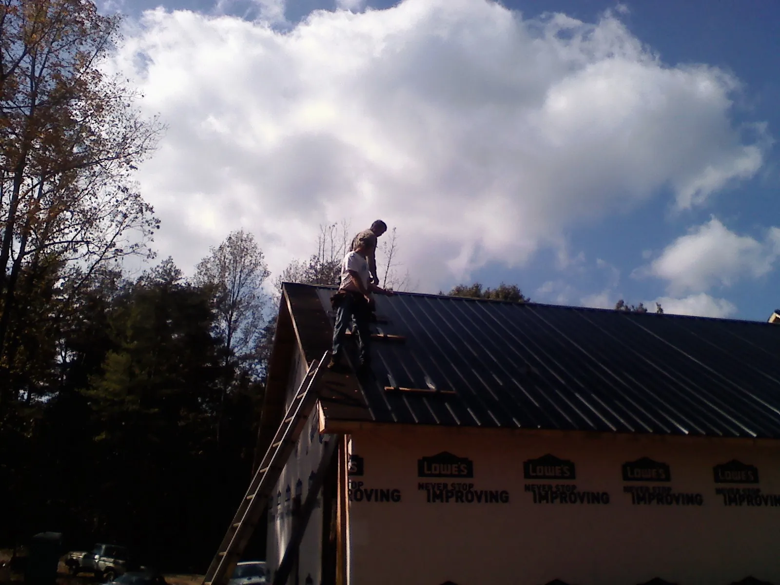Roofer fastening dark metal panels high against a cloudy sky, from a Roof Inspection job in Pawlet