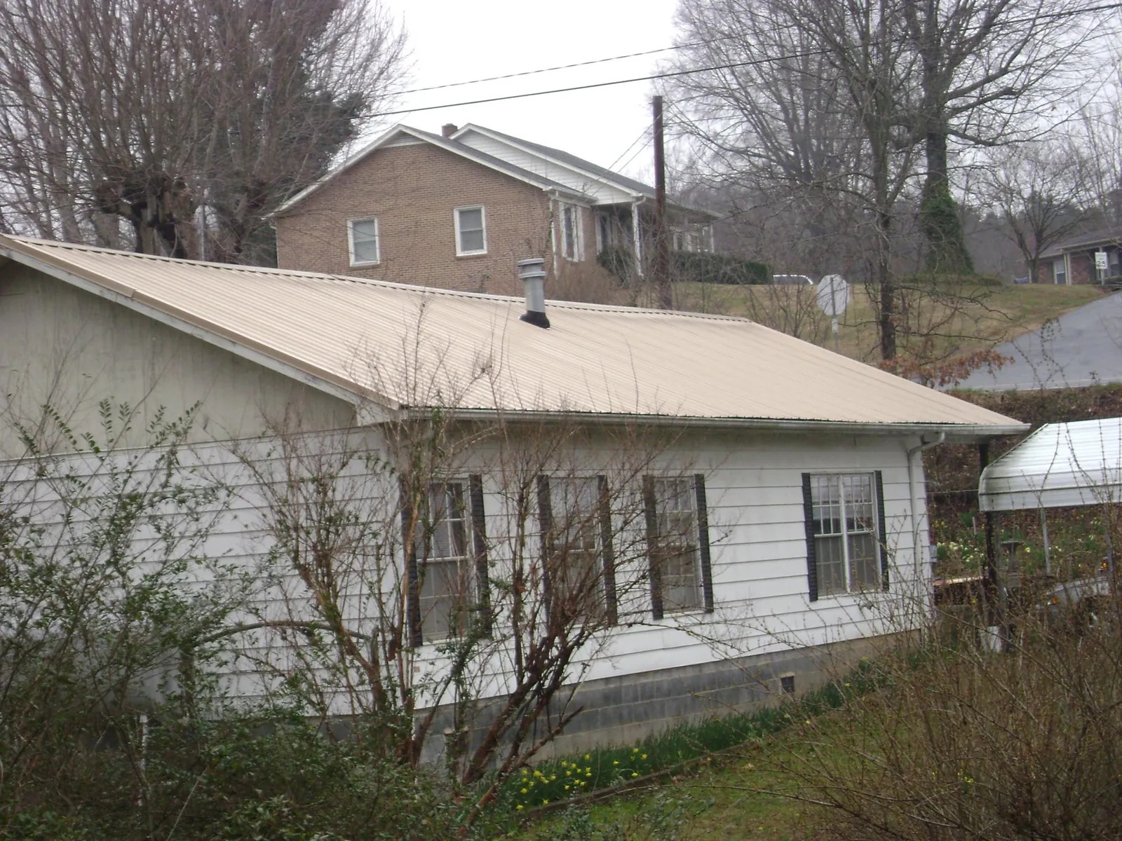 Tan metal roof on a white sided house set into a hillside — Commercial Roofing by Roofing Brothers in Pawlet